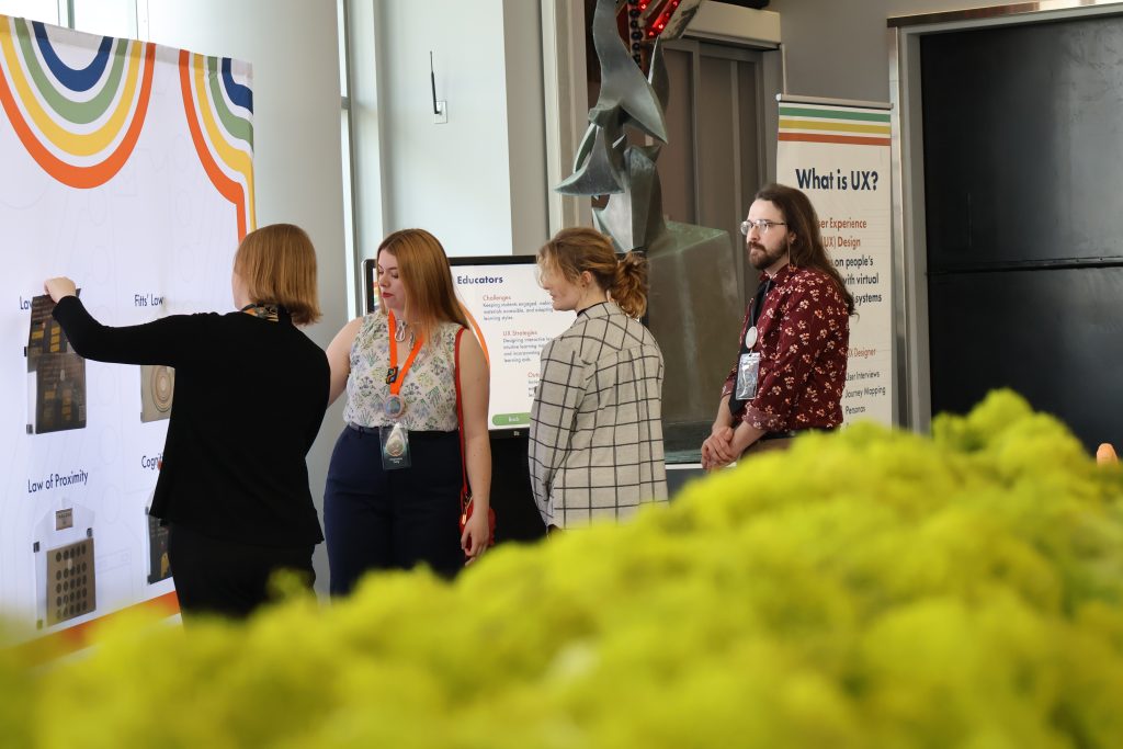 A woman guides three other people through her capstone display.